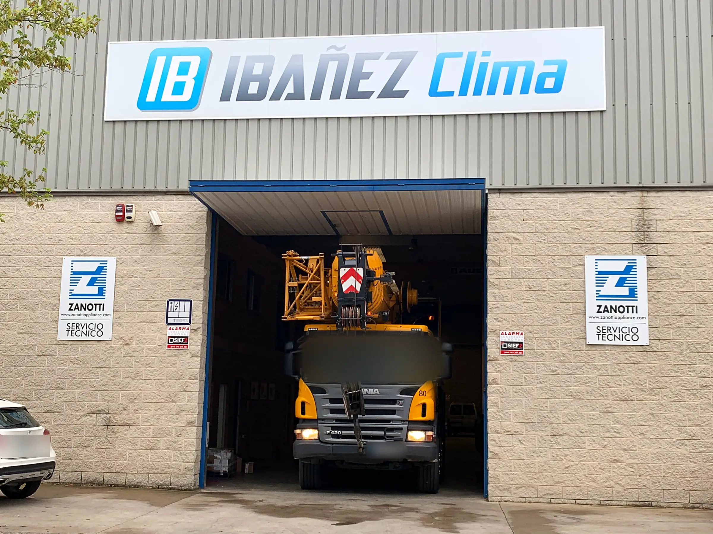 Fachada de la nave de IBAÑEZ CLIMA en Lleida con el rótulo de la empresa y un camión grúa entrando al taller.